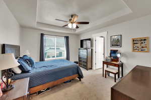 Bedroom featuring a tray ceiling, light carpet, a ceiling fan, and a textured ceiling