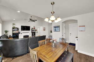 Dining room featuring lofted ceiling, wood finished floors, a chandelier, a fireplace, and arched walkways