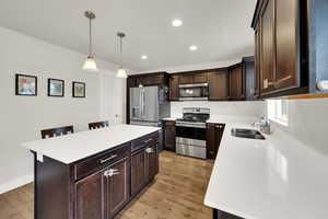 Kitchen featuring dark brown cabinetry, appliances with stainless steel finishes, a kitchen bar, pendant lighting, and recessed lighting
