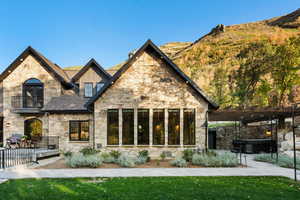 Rear view of house featuring stone siding, a pergola, roof with shingles, and a balcony