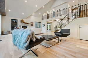 Living room with a fireplace, light wood-style floors, stairway, high vaulted ceiling, and recessed lighting