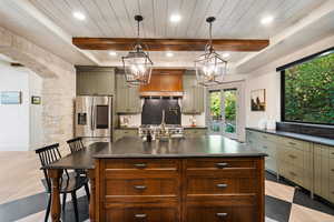 Kitchen with beam ceiling, dark countertops, an island with sink, decorative light fixtures, and decorative backsplash