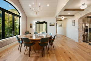 Dining area with light wood-type flooring, healthy amount of natural light, arched walkways, a chandelier, and beamed ceiling