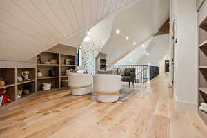 Sitting room with built in features, an upstairs landing, light wood finished floors, lofted ceiling, and wood ceiling