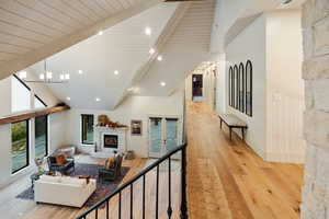 Living room with a glass covered fireplace, beam ceiling, light wood finished floors, high vaulted ceiling, and a chandelier