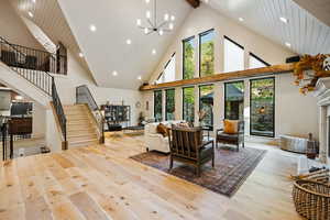 Living room with stairs, high vaulted ceiling, light wood-type flooring, beamed ceiling, and a fireplace