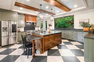 Kitchen featuring stainless steel appliances, decorative light fixtures, custom exhaust hood, dark flooring, and an island with sink