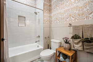 Full bath with shower / bath combination with curtain and wainscoting