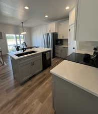 Kitchen with gray cabinetry, hanging light fixtures, black appliances, dark wood finished floors, and light stone counters