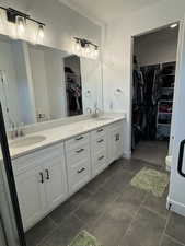 Bathroom with a walk in closet, double vanity, and dark tile patterned floors