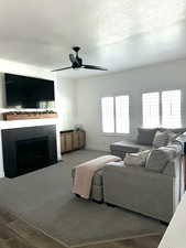 Living room with wood finished floors, a fireplace with flush hearth, a textured ceiling, and ceiling fan