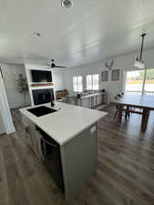 Kitchen featuring a fireplace, gray cabinetry, a textured ceiling, dark wood-style flooring, and an island with sink