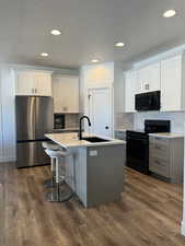 Kitchen featuring gray cabinetry, black appliances, a center island with sink, a textured ceiling, and dark wood-style flooring