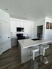Kitchen featuring backsplash, dark wood finished floors, black / electric stove, an island with sink, and stainless steel microwave