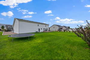 View of green lawn with a trampoline, a patio area, and a residential view