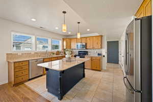 Kitchen with stainless steel appliances, backsplash, decorative light fixtures, light stone counters, and a kitchen island