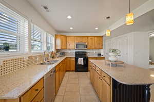 Kitchen with backsplash, light stone countertops, decorative light fixtures, light tile patterned floors, and stainless steel appliances