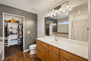 Full bath with a spacious closet, vanity, dark wood-style floors, and curtained shower