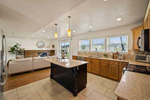 Kitchen featuring light stone counters, decorative light fixtures, a textured ceiling, backsplash, and brown cabinets