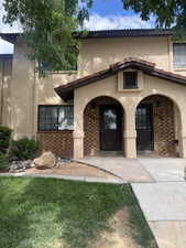 View of exterior entry with stucco siding, covered porch, brick siding, and a yard