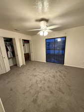 Unfurnished bedroom featuring carpet flooring, a textured ceiling, a ceiling fan, and two closets