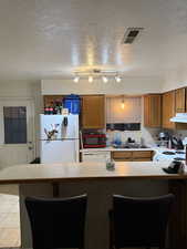Kitchen with a breakfast bar area, brown cabinetry, light countertops, a textured ceiling, and a peninsula