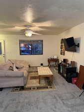 Living area featuring a textured ceiling, carpet flooring, and a ceiling fan