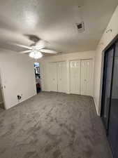 Unfurnished bedroom featuring two closets, carpet flooring, a textured ceiling, and a ceiling fan