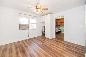 Empty room with wood finished floors, a ceiling fan, and cooling unit
