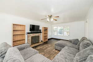 Living area featuring ornamental molding, dark wood-style floors, a stone fireplace, and ceiling fan