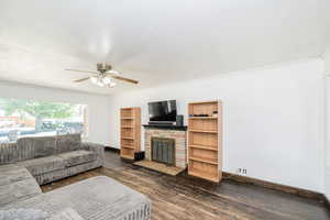 Living area featuring dark wood finished floors, ornamental molding, a stone fireplace, and ceiling fan