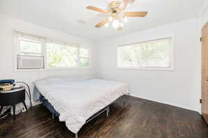 Bedroom featuring multiple windows, dark wood-style floors, and a ceiling fan