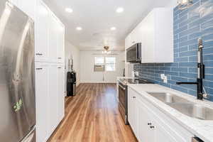 Kitchen with appliances with stainless steel finishes, white cabinets, light stone counters, decorative backsplash, and light wood-type flooring