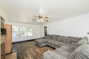 Living area with dark wood-type flooring, ornamental molding, a ceiling fan, and a fireplace