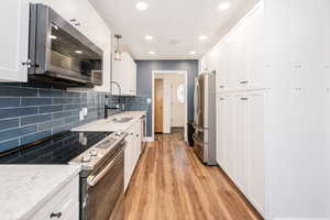 Kitchen with appliances with stainless steel finishes, decorative backsplash, white cabinets, light stone counters, and light wood finished floors