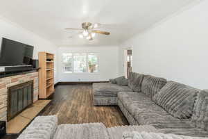 Living area featuring dark wood-type flooring, ornamental molding, a fireplace, and ceiling fan
