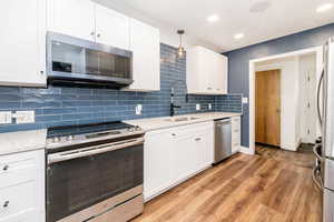 Kitchen featuring stainless steel appliances, white cabinets, decorative backsplash, light wood finished floors, and recessed lighting