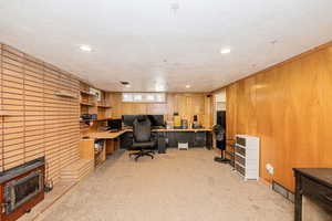 Home office with a textured ceiling, light colored carpet, wooden walls, and recessed lighting