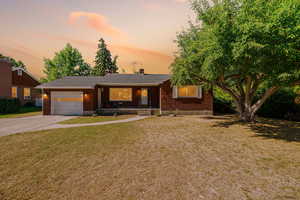 Single story home featuring brick siding, driveway, a chimney, an attached garage, and covered porch