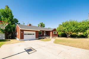 Single story home featuring concrete driveway, a front lawn, a garage, brick siding, and a chimney