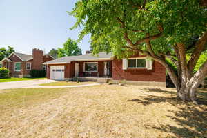Ranch-style home featuring concrete driveway, brick siding, a garage, and a front yard