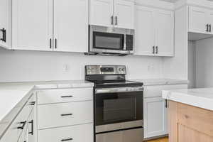 Kitchen featuring appliances with stainless steel finishes, white cabinets, and light stone countertops