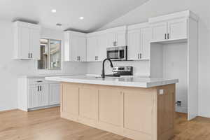 Kitchen featuring recessed lighting, light wood-type flooring, an island with sink, stainless steel appliances, and lofted ceiling