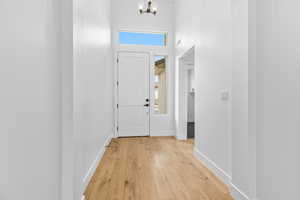 Foyer entrance featuring healthy amount of natural light, light wood finished floors, a towering ceiling, and a chandelier