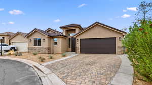 View of front of house with stone siding, stucco siding, decorative driveway, a garage, and a tile roof