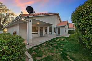 Back of property featuring a patio area, a lawn, stucco siding, and a tiled roof