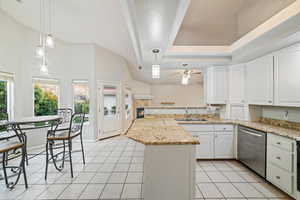Kitchen with light tile patterned flooring, white cabinets, light stone countertops, dishwasher, and a peninsula