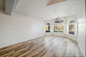 Unfurnished dining area featuring lofted ceiling, wood finished floors, and a textured ceiling