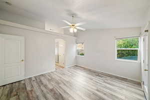 Spare room featuring vaulted ceiling, arched walkways, light wood-type flooring, and ceiling fan
