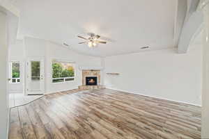 Unfurnished living room with lofted ceiling, a ceiling fan, light wood-type flooring, and a fireplace